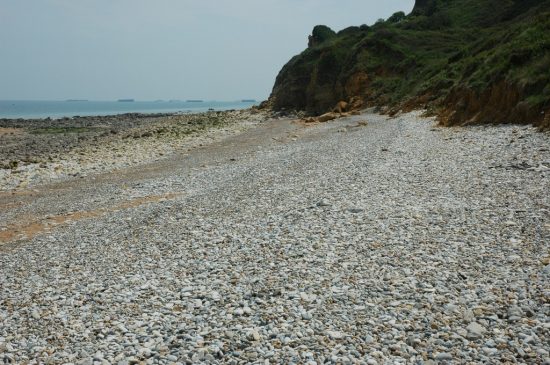 Renske Cramer Creatief foto van een kiezelstrandje aan de Normandische kust. Op de achtergrond ziet u in zee nog resten van betonnen pontons, die de geallieerden hebben gebruikt tijdens D-Day. e kust in de Basse-Normandie (Frankrijk)